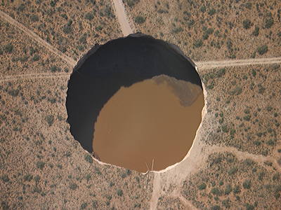 Figure 9.22: This sinkhole near Carlsbad, New Mexico formed after improper solution mining practices created a large cavity beneath the desert. Three days after its collapse, the sinkhole was 200 meters (670 feet) long and 140 meters (450 feet) wide, and there are major concerns that it could expand into the town of Carlsbad.