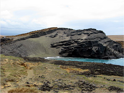 Figure 4.26: Mahana littoral cone on Hawai’i Island, now breached by the ocean. The tephra here contains abundant olivine crystals that erode to form a “green sand beach.”